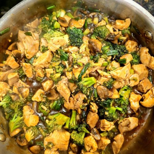 High protein chicken broccoli and mushroom stir fry in a savory brown sauce, cooked in a stainless steel pan.