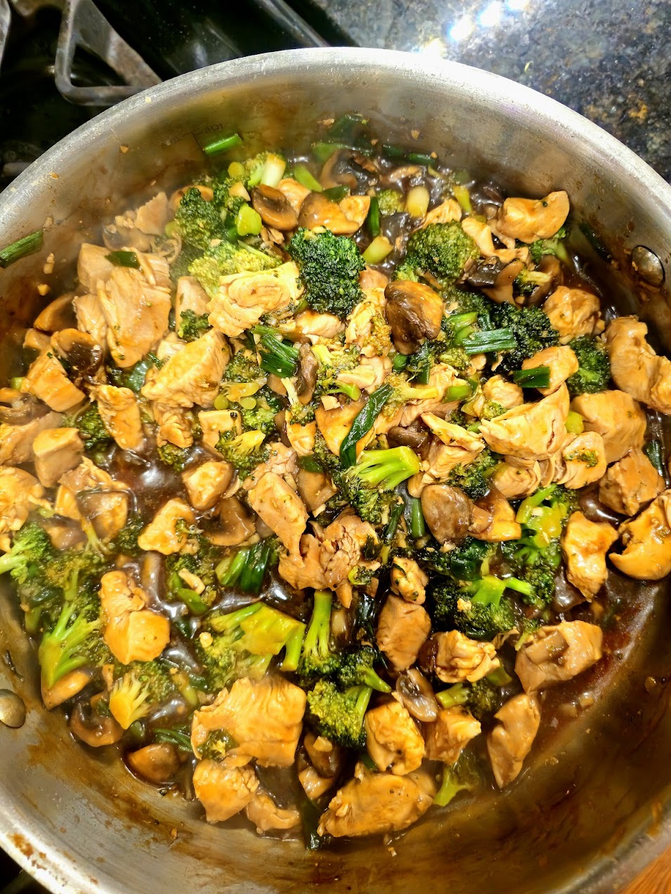 High protein chicken broccoli and mushroom stir fry in a savory brown sauce, cooked in a stainless steel pan.