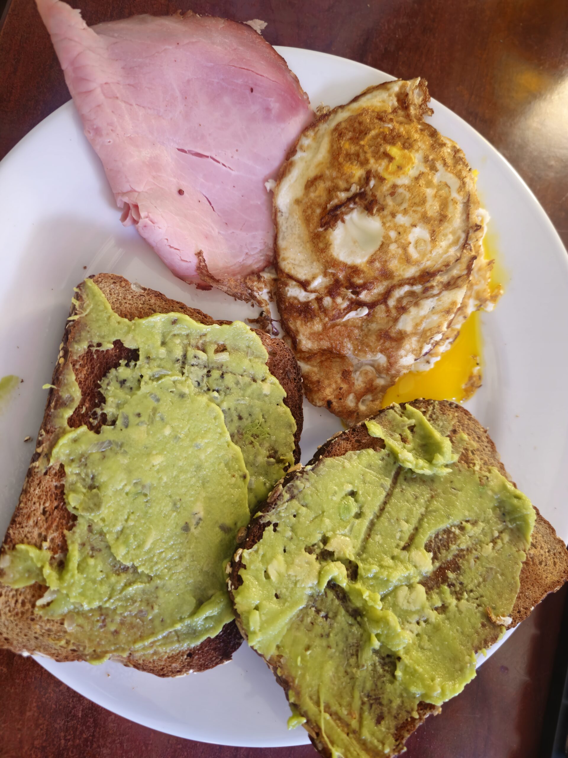 Two slices of whole wheat avocado toast served with crispy fried eggs and lean ham for a high-protein breakfast.