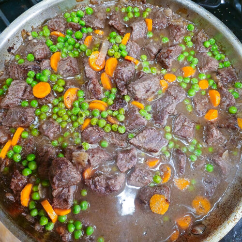 Lean beef stew with peas and carrots simmering in a red wine and bone broth reduction, prepared for a high-protein recovery meal.