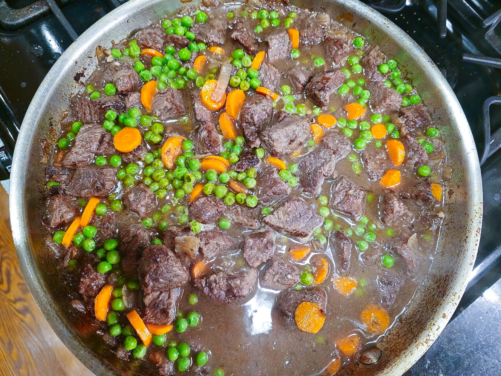 Lean beef stew with peas and carrots simmering in a red wine and bone broth reduction, prepared for a high-protein recovery meal.